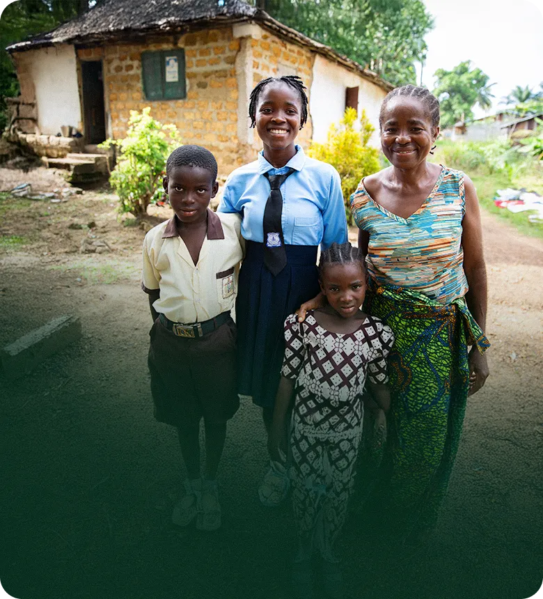 흙집 앞에서 교복을 입은 아이들과 함께 밝게 웃고 있는 사람들의 모습