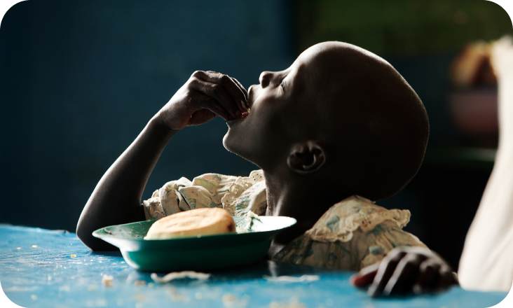 탁자에 그릇이 올려져 있고, 그릇안에 빵을 맨손으로 먹고 있는 어린아이의 모습