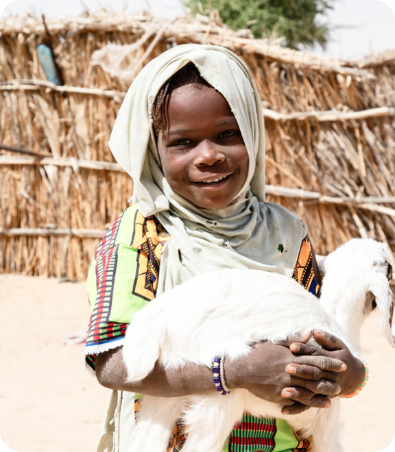 머리에 스카프를 두르고 흰 염소를 안고 환하게 웃는 아이