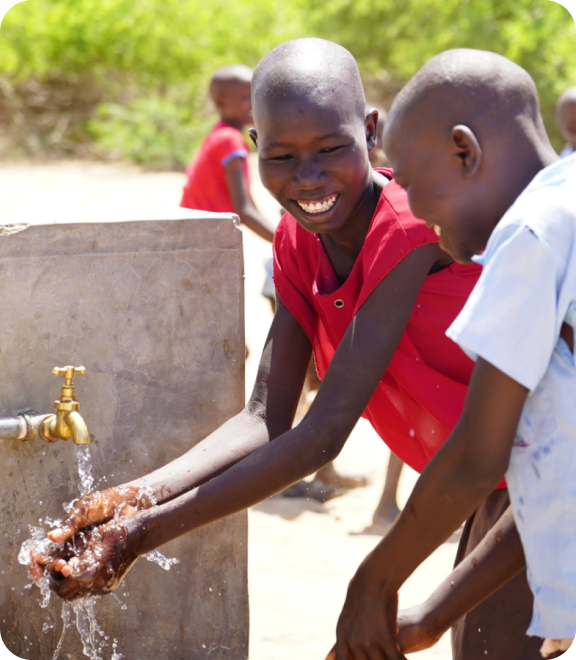 야외 수도에서 손을 씻으며 환하게 웃고 있는 두 아이들
